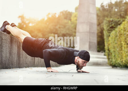 Giovane sportivo barbuto fa di allenamento in un parco, facendo una serie di Ups push all'aperto. Foto Stock