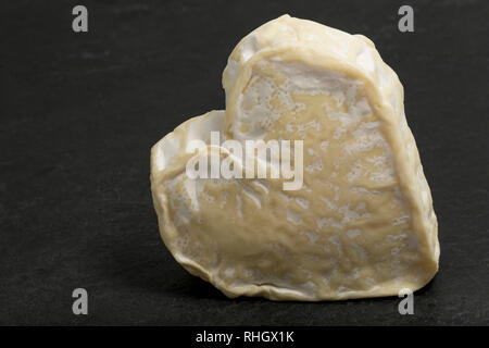 A heart-shaped Neufchatel formaggio, in Normandia, Francia realizzato dal latte di mucca, fotografato su un oscuro, ardesia sfondo. Inghilterra REGNO UNITO GB Foto Stock