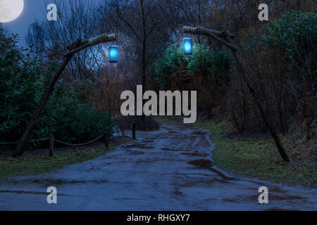 Terreni fangosi strada forestale di notte illuminata con lanterne appese su pali di legno, fantasia o scena spooky Foto Stock