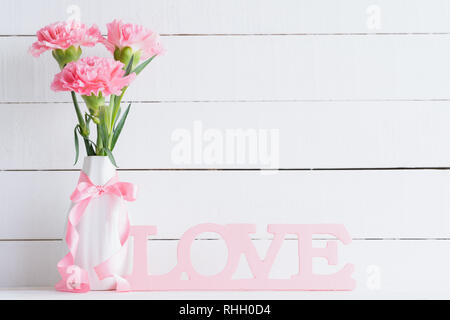 Il giorno di San Valentino e il concetto di amore. Rosa fiori di garofano in vaso di legno con lettere che compongono la parola amore scritta su sfondo bianco. Foto Stock