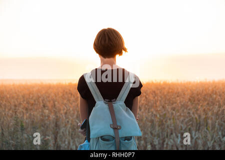 Retroilluminato con la figura di una donna godendo del tramonto luminoso. Persona di sesso femminile in piedi di sera la luce del sole in un campo Foto Stock