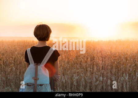 Retroilluminato con la figura di una donna godendo del tramonto luminoso. Persona di sesso femminile in piedi di sera la luce del sole in un campo Foto Stock