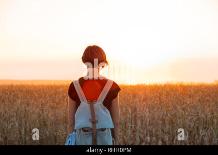 Retroilluminato con la figura di una donna godendo del tramonto luminoso. Persona di sesso femminile in piedi di sera la luce del sole in un campo Foto Stock