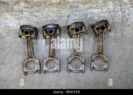 Quattro metallo argentato pistoni automobilistici in cattivo stato rimosso dal motore usato in un deposito di olio giacente sul cemento in un veicolo officina per riparazione di washi Foto Stock