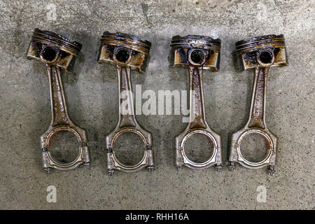 Quattro metallo argentato pistoni automobilistici in cattivo stato rimosso dal motore usato in un deposito di olio giacente sul cemento in un veicolo officina per riparazione di washi Foto Stock