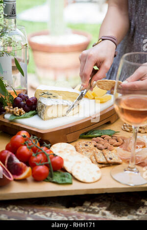 Mani femminili cuneo di taglio di formaggio su marmo di formaggi, con salumi e vino a picnic. Foto Stock