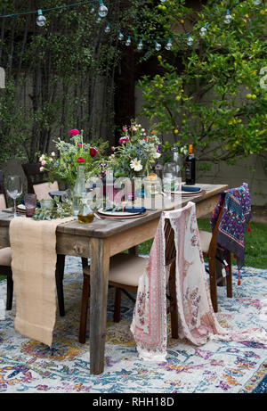 Cortile esterno dinner party messa in tavola con fiori, inserire le impostazioni, stringa di luci e tessuto. Foto Stock