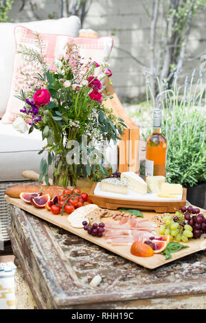 Scheda di formaggio con salumi e fiori sul cortile esterno partito picnic con vino e tavolo da caffè. Foto Stock