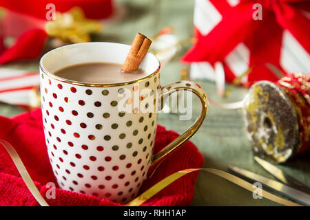 Oro polka dot tazza di cioccolata calda con la stecca di cannella tra vacanze di Natale di colore rosso e bianco della carta da imballaggio e il nastro di inchiostro sulla superficie verde. Foto Stock