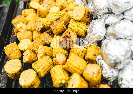 I tutoli di mais e patate avvolte in pellicola di alluminio su un barbecue. Foto Stock