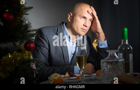 Giovane triste festeggia il nuovo anno a casa da soli seduti a tavola festiva con bicchiere di vino Foto Stock