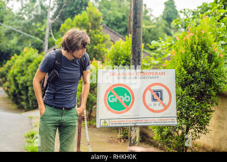 BALI, Indonesia - 21 Maggio 2018: il giovane uomo guarda in segno di protesta su una parete in indonesiano opponendosi alla Uber e afferrare i tassisti si legge 'uber e Grab Foto Stock