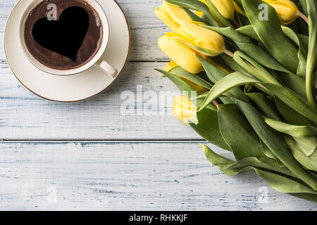 Parte superiore della vista modulo di tazza di caffè con il cuore e la molla tulipani su un tavolo di legno. Foto Stock