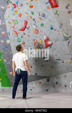 Rocciatore si alza e guarda la parete di arrampicata con ganci in boulder hall Foto Stock