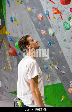 Rocciatore si alza e guarda la parete di arrampicata con ganci in boulder hall Foto Stock
