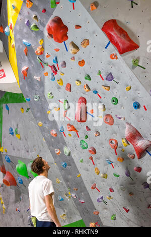 Rocciatore si alza e guarda la parete di arrampicata con ganci in boulder hall Foto Stock