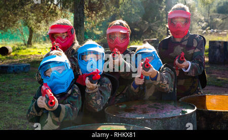 Gentile felice allegro sorriso positivo gruppo di bambini paintball giocatori in camuffamento in posa con pistole di paintball sul campo da gioco all'aperto Foto Stock