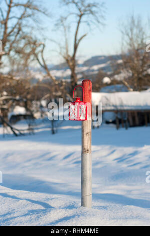 Lanterna rossa appesa sul montante in legno. Inverno giornata di sole. Al di fuori di lanterna metallico per l'illuminazione. Vista ravvicinata di una lanterna in snow Foto Stock