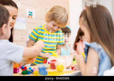 I bambini giocano di pasta in asilo nido. I bambini con insegnante lo stampo da plastilina in asilo nido. Poco gli studenti impastare la creta per modellare con le mani in età prescolare. Foto Stock