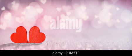 Due piccoli fatti a mano in legno rosso cuori in rosa luminoso luci sfondo bokeh di fondo Foto Stock