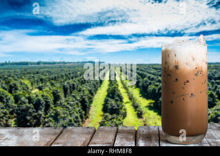 Un bicchiere di caffè ghiacciato sul tavolo di legno con la piantagione di caffè,cielo blu sullo sfondo. Foto Stock