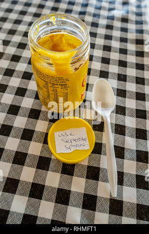 Colmans senape inglese vaso con coperchio e cucchiaio di plastica su un bianco e nero in plastica tabella gingham stoffa su un tavolo del bar in Inghilterra Foto Stock