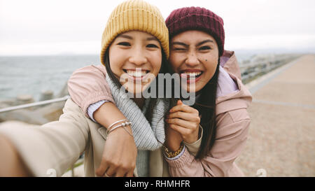 Sorridente donne asiatiche in piedi all'aperto azienda ogni altro in una mattinata d'inverno. Allegro donne asiatiche in inverno indossare divertirsi facendo facce nea permanente Foto Stock