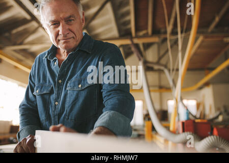 Senior misure falegname legno, verificarne la rettilineità. Maschio maturo falegname preparazione mobili nella sua bottega. Foto Stock