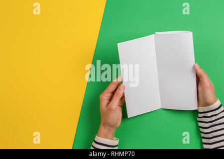 Donna mani tenendo vuoto bianco brochure flyer opuscolo. Mockup modello di foglio opuscolo pubblicitario sul verde e sfondo giallo Foto Stock