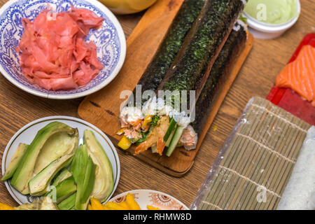 Effettua il sushi e panini a casa. Piastre con ingredienti per il tradizionale cibo giapponese e sushi rotoli sulla tavola di legno sul tavolo da cucina, vista da abov Foto Stock