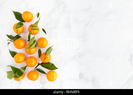 La disposizione delle clementine con foglie su marmo bianco lo sfondo con un sacco di spazio copia. Vista dall'alto. Foto Stock