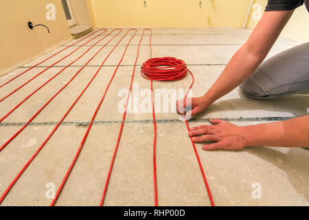 Elettricista installazione di riscaldamento elettrico rosso il filo del cavo sul pavimento di cemento in camera incompiuto. Ristrutturazione e costruzione, confortevole casa calda concep Foto Stock