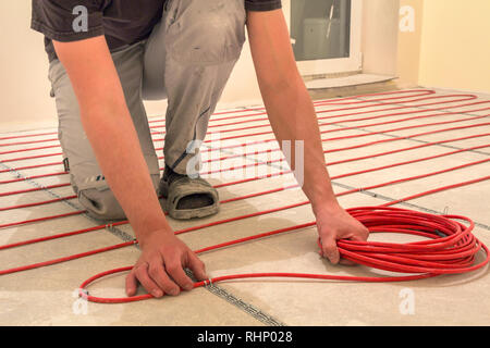 Elettricista installazione di riscaldamento elettrico rosso il filo del cavo sul pavimento di cemento in camera incompiuto. Ristrutturazione e costruzione, confortevole casa calda concep Foto Stock