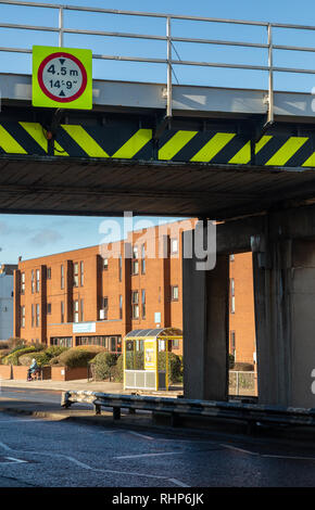 Fluorescente cartello segnaletico rosso con bordo circolare e in bianco e nero e giallo iscrizioni indicanti un basso ponte ferroviario con il limite di altezza Wallasey Village feb. Foto Stock