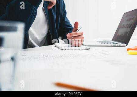 Ritratto di imprenditore seduta a tavola utilizzare il laptop e il blocco note in Spazio Office. Giovane studente maschio preparo il progetto Foto Stock