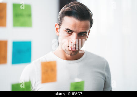 Uomo Creativo scrivendo una nota adesiva sulla parete di vetro presso lo spazio in ufficio. Il brainstorming Manager nuove startup business Foto Stock