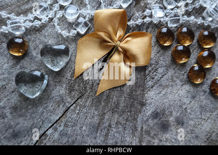 Shiny golden bow, trasparente cuori e perle sulla sfondo irregolare di un vecchio ceppo con una fessura Foto Stock