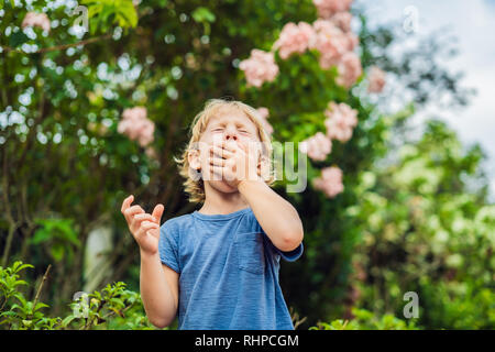 Little Boy starnuto nel parco sullo sfondo di un albero di fioritura. Allergia ai pollini concept Foto Stock