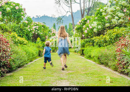 Madre e figlio sono in funzione circa nel giardino fiorito. Felice vita familiare il concetto di stile Foto Stock