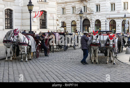 Carrozze trainate da cavalli in attesa per i turisti di fronte al Palazzo di Hofburg sulla Michaelerplatz a Vienna, in Austria Foto Stock