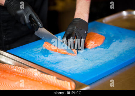 Cucina a tema è una professione di cottura. Close-up di un uomo caucasico la mano in un ristorante di cucina Preparazione di filetti di pesce rosso salmone carne in black l Foto Stock