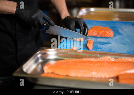 Cucina a tema è una professione di cottura. Close-up di un uomo caucasico la mano in un ristorante di cucina Preparazione di filetti di pesce rosso salmone carne in black l Foto Stock