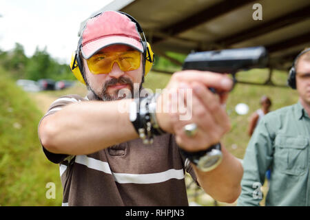 L uomo riprese su un esterno di tiro. Maschio pistola di puntamento al poligono di tiro. Tempo libero attivo. Foto Stock