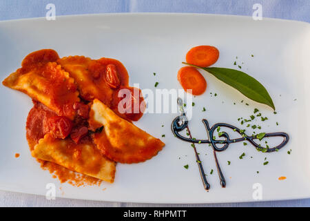 Ravioli in salsa di pomodoro su una piastra bianca, con una chiave di violino design nella riduzione di balsamico. Foto Stock