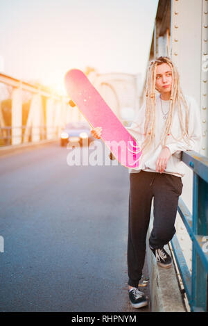 Giovane donna ritratto con lo skateboard su bridge Foto Stock