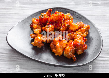 Il coreano cucina Cinese - Kkanpunggi piccante fritto di pollo a pezzi con verdure in salsa agrodolce sulla piastra nera close up Foto Stock