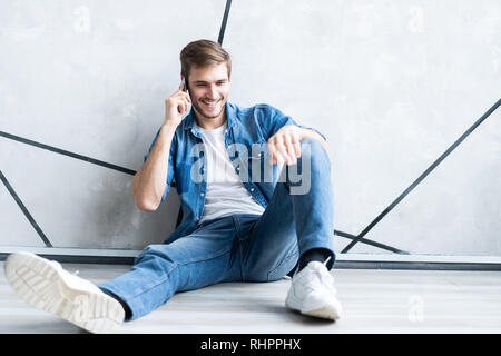 Giovane uomo informale parlando al telefono mentre è sdraiato sul pavimento. Foto Stock