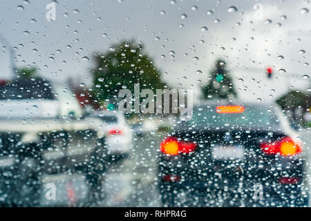 Le gocce di pioggia sul parabrezza in un giorno di pioggia; vetture fermo ad un semaforo in background; California Foto Stock