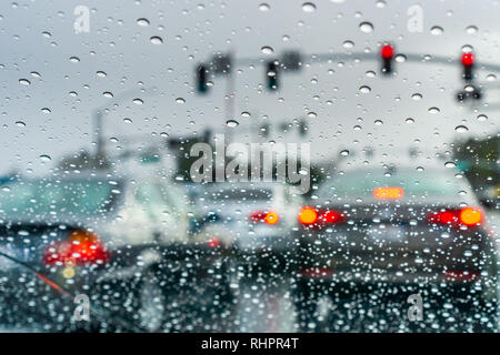 Le gocce di pioggia sul parabrezza in un giorno di pioggia; vetture fermo ad un semaforo in background; California Foto Stock