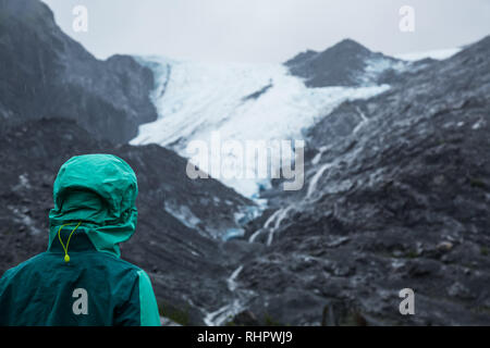 Rainy day presso il Ghiacciaio di Worthington con la donna in verde Giacca pioggia e il cofano guardando verso il ghiacciaio in Alaska Foto Stock
